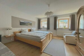 A bedroom with a wooden bed, a bedside table, a chair, a radiator, and a window with curtains. - Holiday apartment with 4 bedrooms (Mittenwald)