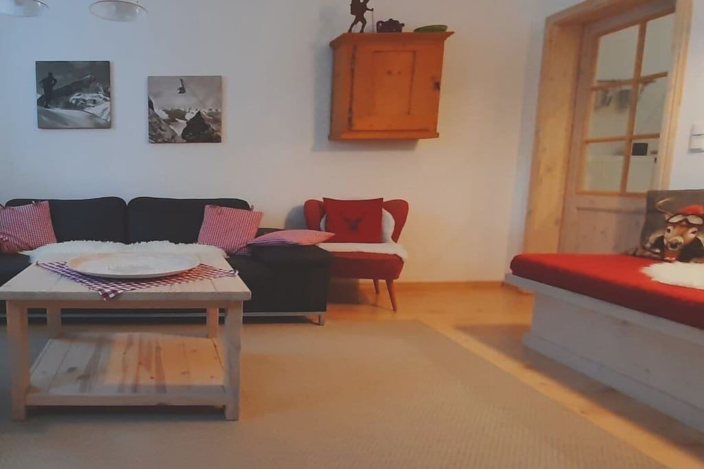Ein Wohnzimmer mit einer Couch, einem roten Sessel, einem Holztisch und einem Schrank.