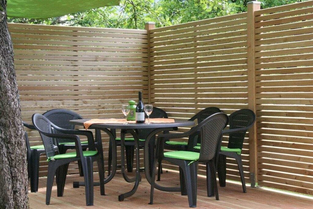 An outdoor patio with a wooden fence, a round table, and black chairs with green cushions.