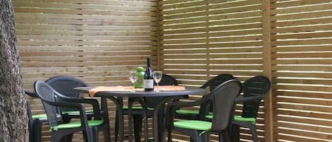 An outdoor patio with a wooden fence, a round table, and black chairs with green cushions.