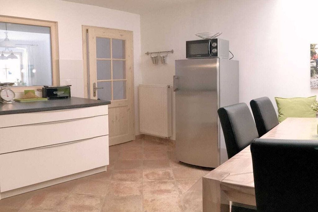 A compact kitchen with a refrigerator, microwave, and a dining table with chairs.