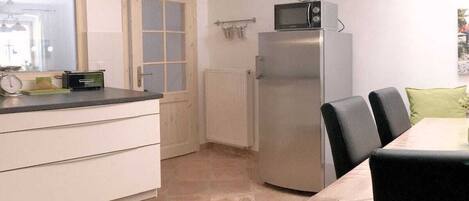 A compact kitchen with a refrigerator, microwave, and a dining table with chairs.