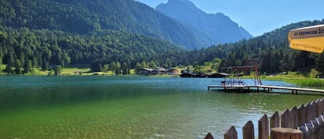 A lake with a wooden dock, surrounded by forested mountains and a clear sky.