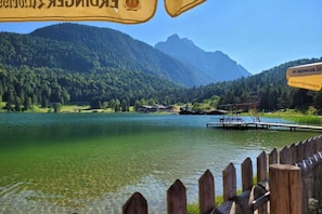 Un lago con un muelle de madera, rodeado de montañas boscosas y un cielo despejado.