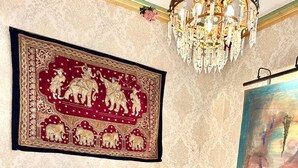 A bed with a quilt, a chandelier, a framed tapestry, and a lamp.