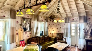 A room with a high ceiling, floral wallpaper, a sofa, a table with a vase, and a chandelier.