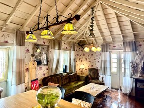 A room with a high ceiling, floral wallpaper, a sofa, a table with a vase, and a chandelier.