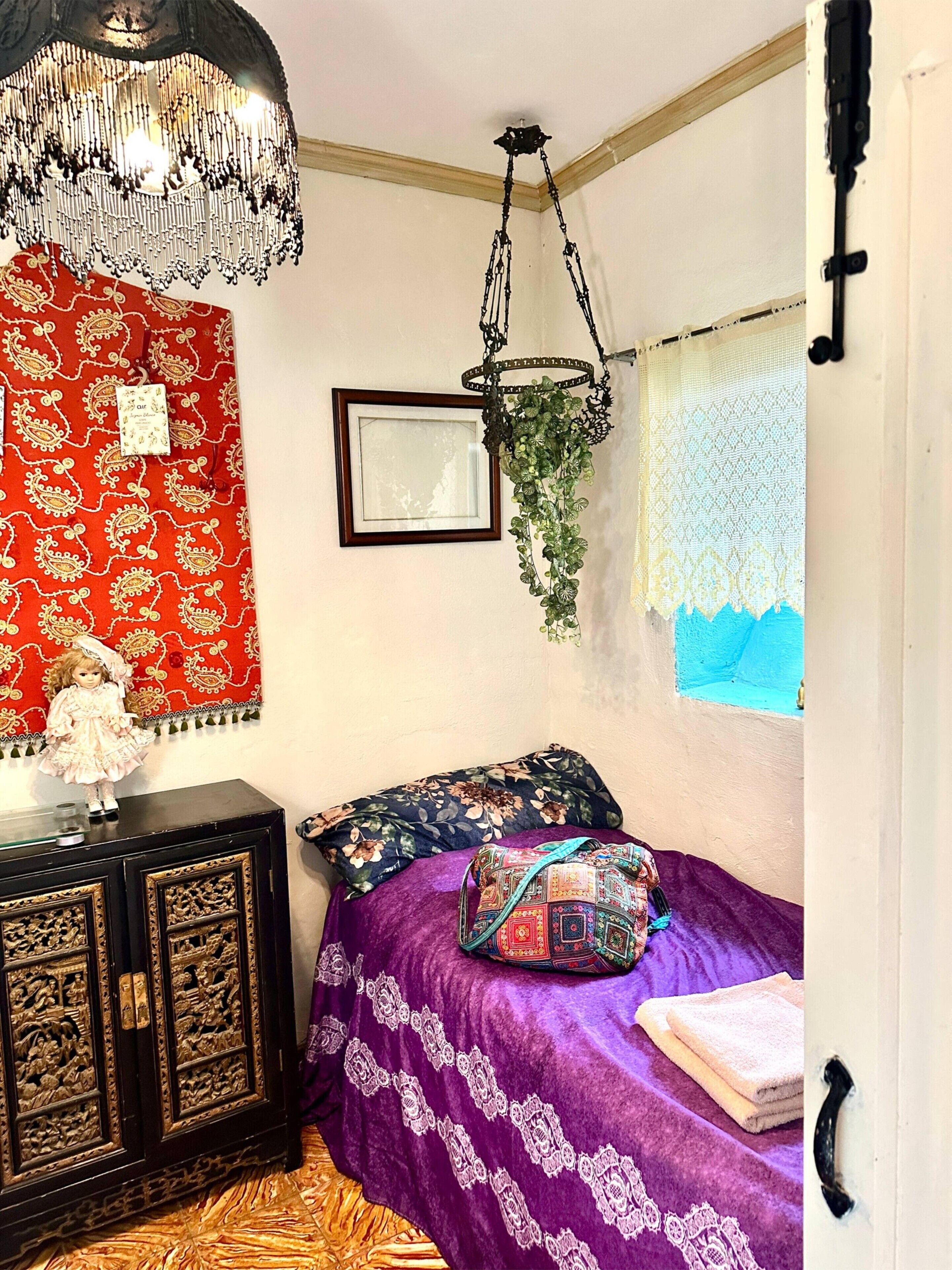 Una habitación con una cama, una planta colgante, un cuadro enmarco y una lámpara decorativa.