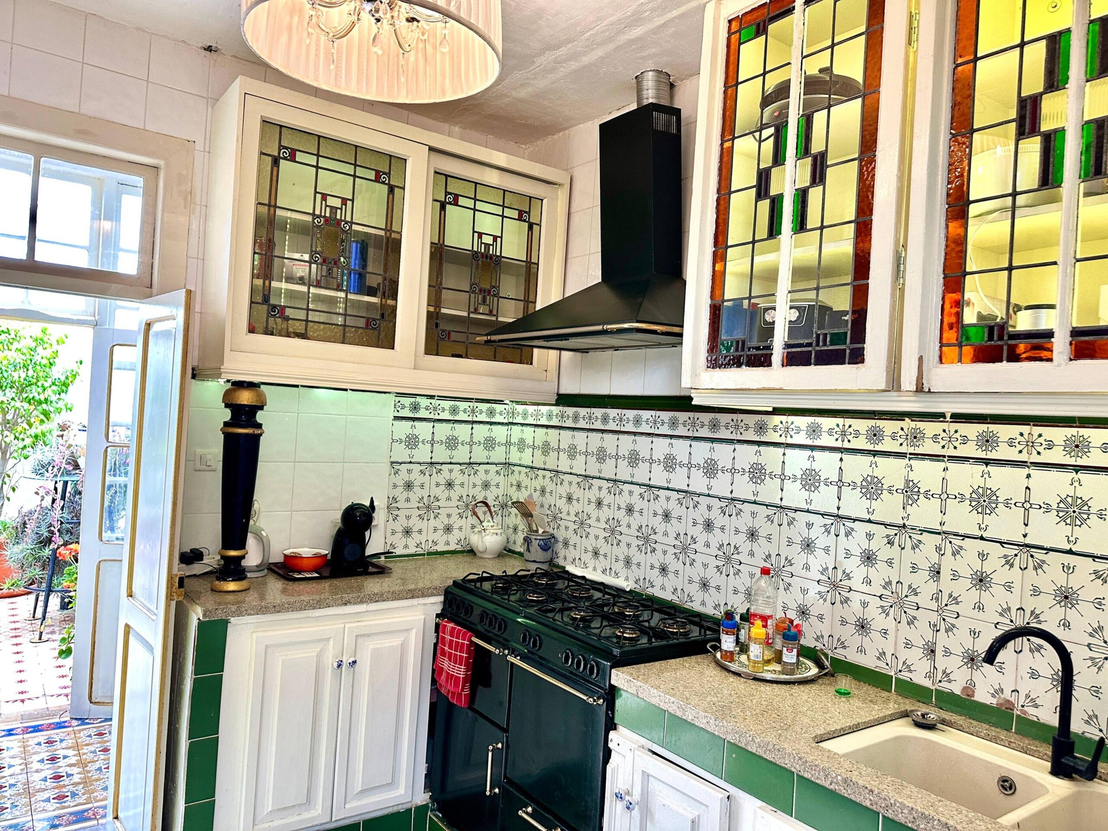 A kitchen with a gas stove, a sink, and a window with stained glass.