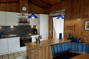 A compact kitchen with a sink, stove, and cabinets, a dining area with a bench, and a clock on the wall. - Holiday home with 1 bedroom (Otterndorf)