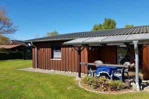 A wooden building with a covered patio area, a window, and a table with chairs. - Holiday home with 1 bedroom (Otterndorf)