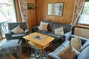 Een gezellige woonkamer met een grijze zithoek, een houten salontafel en vloerkleden met een patroon.