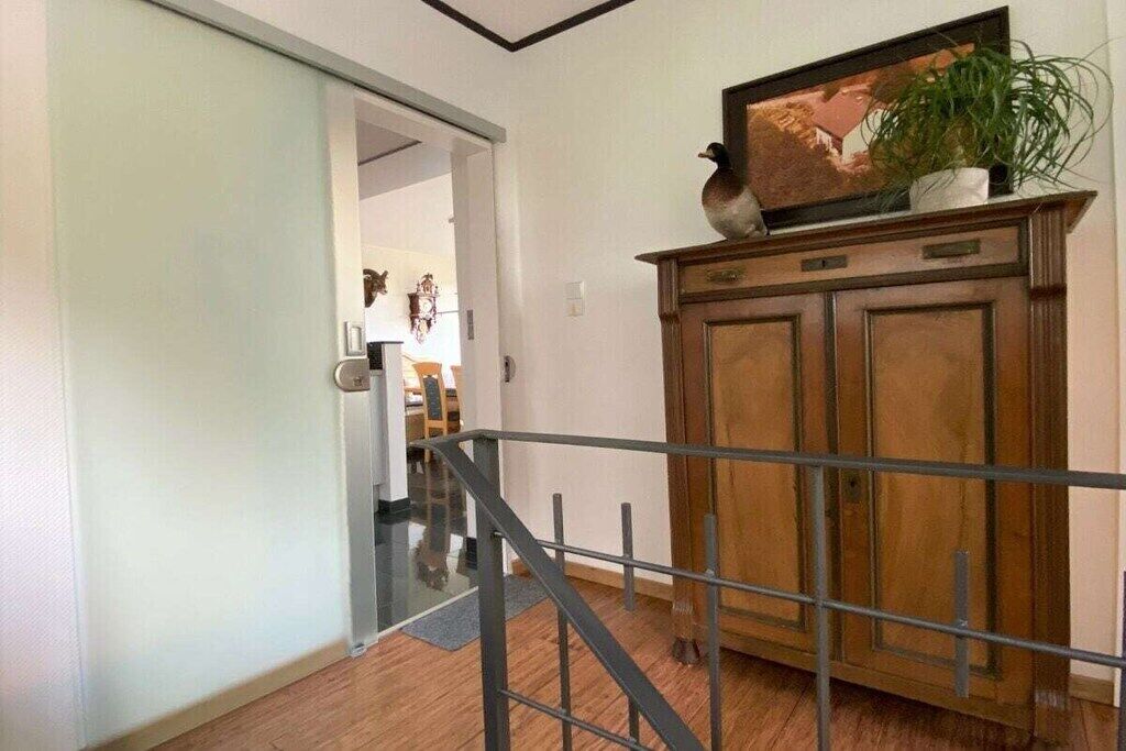 Een gang met een houten kast, een metalen balustrade en een deur naar een andere kamer.