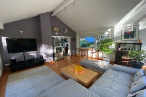 Een moderne woonkamer met een flatscreen televisie, een bank, een salontafel en een eethoek met natuurlijk licht.
