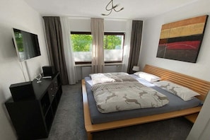 Una camera da letto con un letto, una TV, una cassettiera e una finestra con tende.