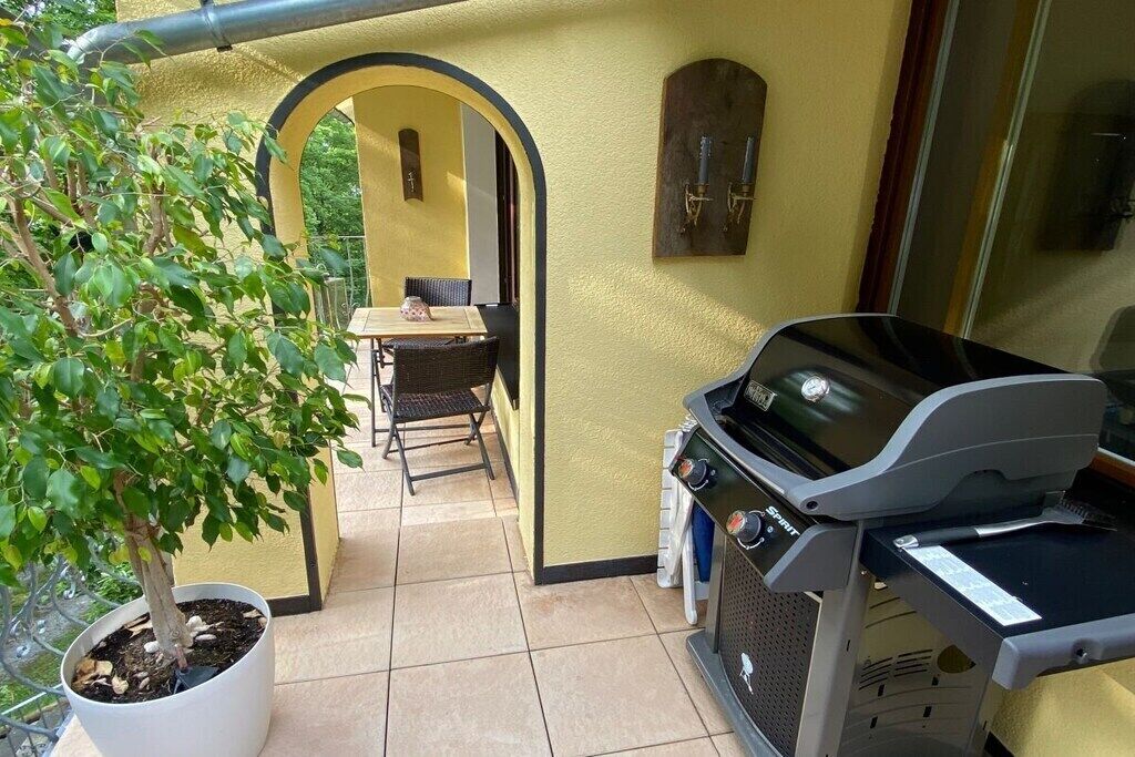 Een terras met een barbecue, een eettafel en stoelen, en een pot met een boom.