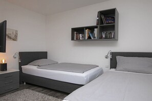 A bedroom with two beds, a bedside table, a wall-mounted bookshelf, and a wall-mounted TV. - Holiday home with 3 bedrooms (Göhren Lebbin)