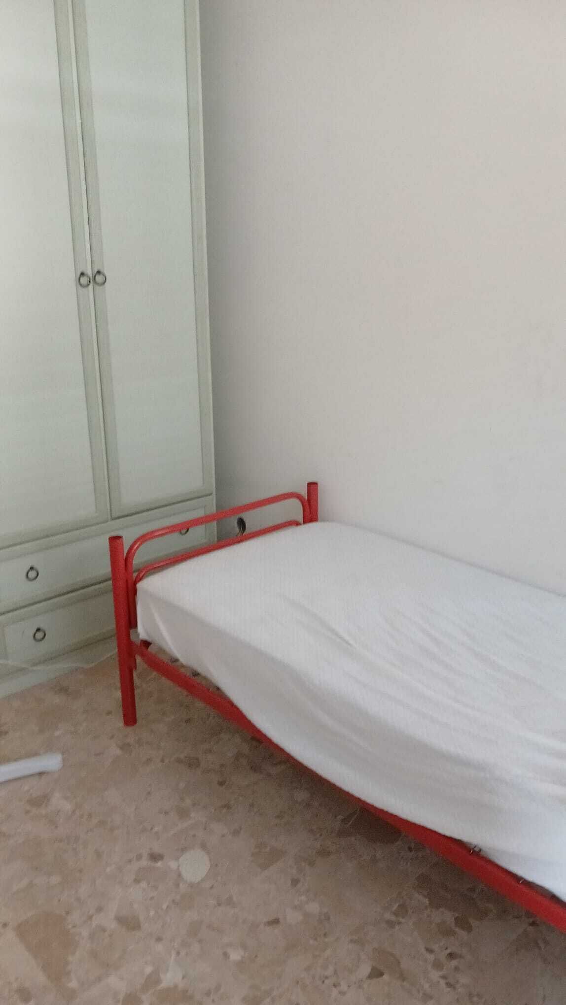 Una habitación con cama individual, armario y suelo de baldosas.