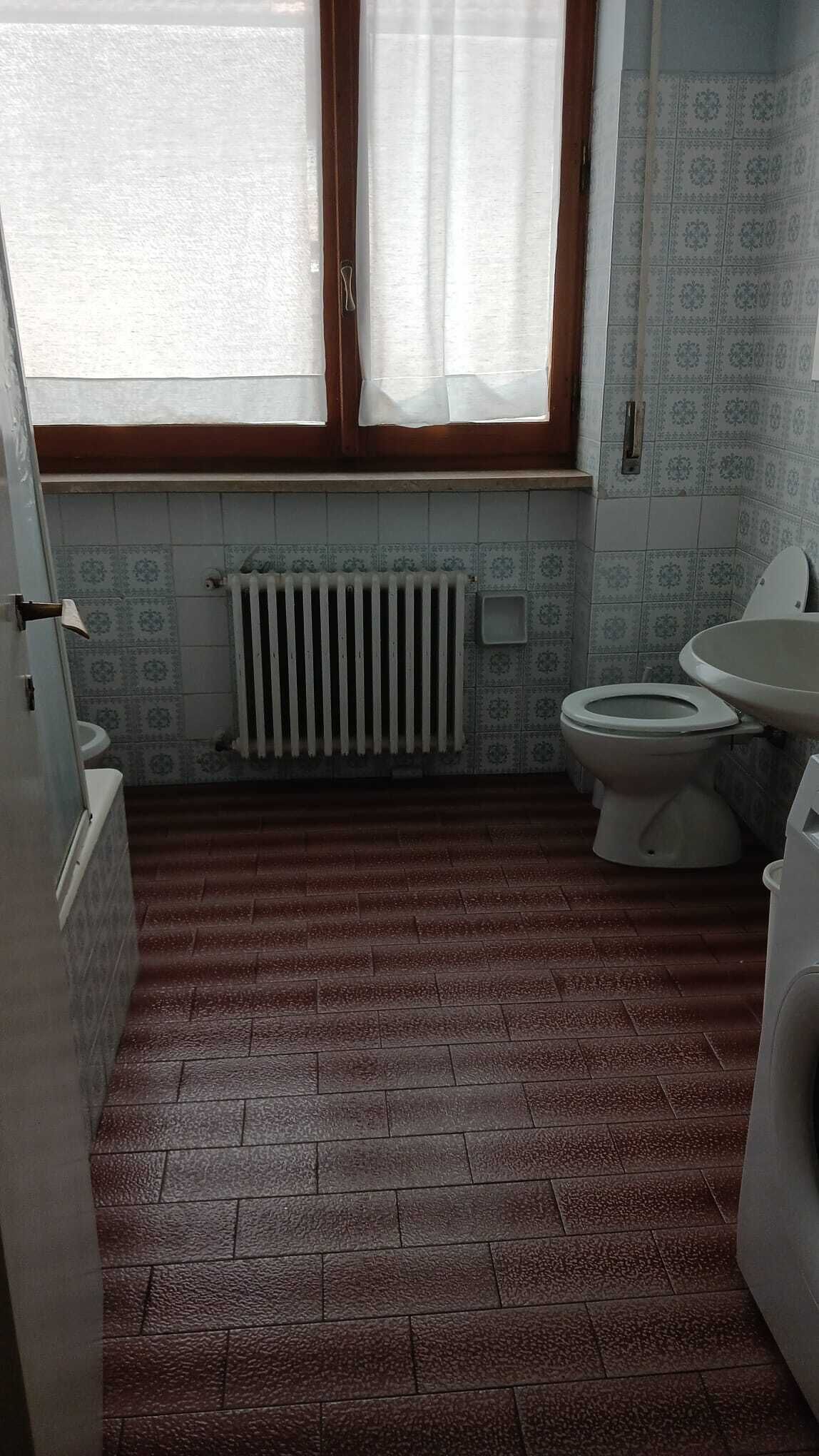 Une salle de bain équipée de toilettes, d’un lavabo, d’un radiateur et d’une fenêtre avec des rideaux.