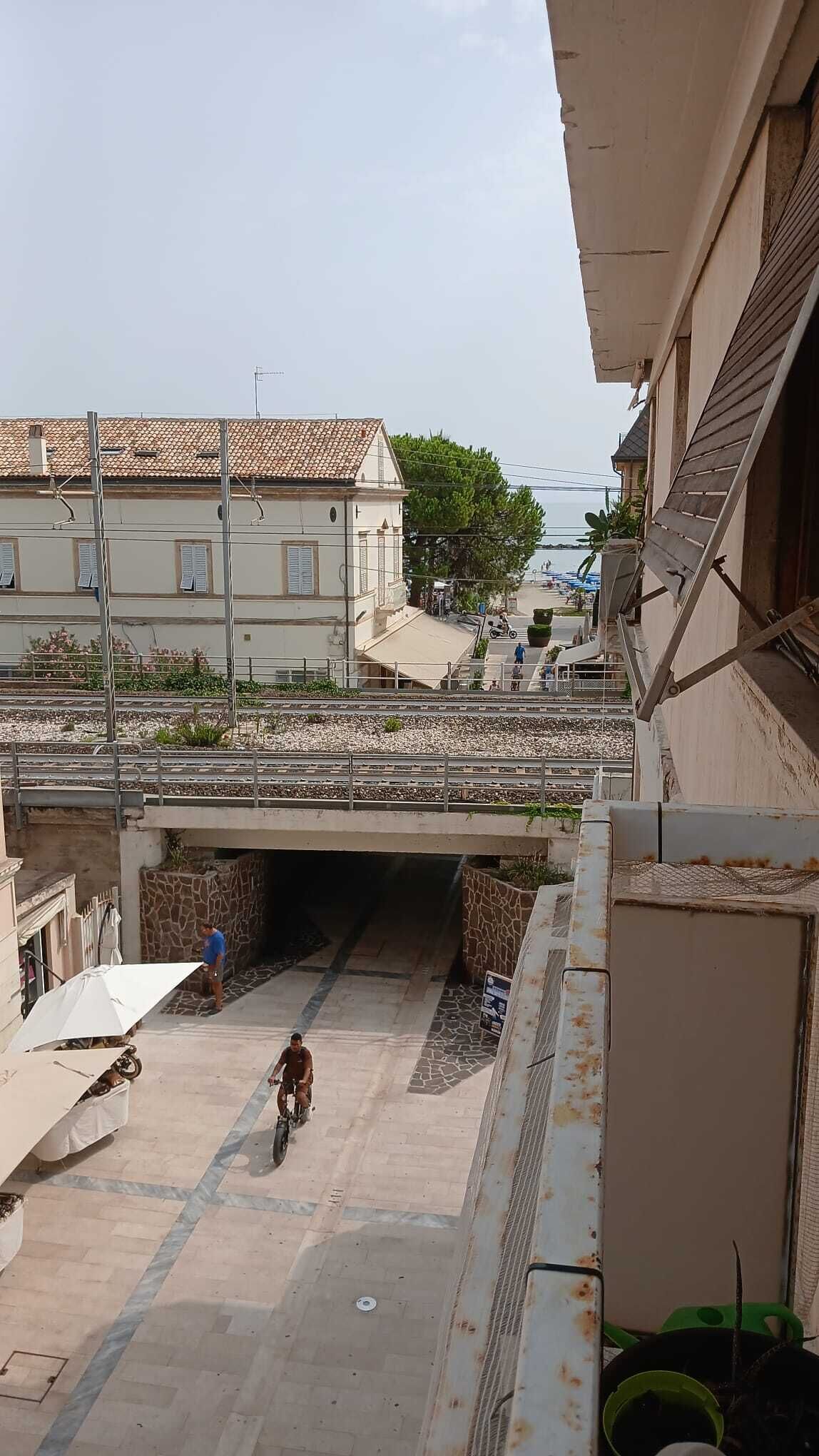 A street view with a pedestrian bridge, a cyclist, and buildings with tiled roofs.