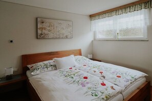 A bedroom with a wooden headboard, a floral bedspread, a bedside table with a lamp, and a window with sheer curtains. - Holiday apartment in Großklein with sauna (Großklein)