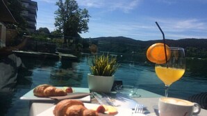 Et spisebord med croissanter og et glas appelsinjuice, med udsigt over vand og et bjerglandskab.