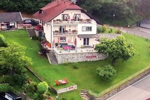 Una casa de dues plantes amb fonaments de pedra, un balcó i una petita zona de jardí.