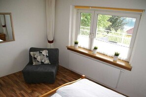 Ein Zimmer mit einem Bett, einem Sessel, einem Fenster mit Pflanzen, einer Heizung und einem Holzboden.