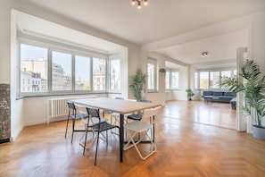 A spacious living area with a large table and chairs, a sofa, and several potted plants. - 3-bedroom apartment ideal for families (Antwerp)