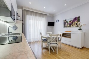 A modern kitchen with a built-in oven, a dining area with a table and chairs, a flat-screen TV mounted on the wall, and a painting of a street scene. - Vatican Flat 2 Bedrooms 2 Ensuite Baths (Roma)