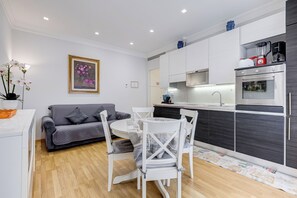 A modern kitchen with white cabinetry, a dining area with a table and chairs, and a gray sofa. - Vatican Flat 2 Bedrooms 2 Ensuite Baths (Roma)