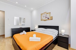 A hotel room with a bed, a nightstand, a dresser, and a wall-mounted artwork. - Vatican Flat 2 Bedrooms 2 Ensuite Baths (Roma)