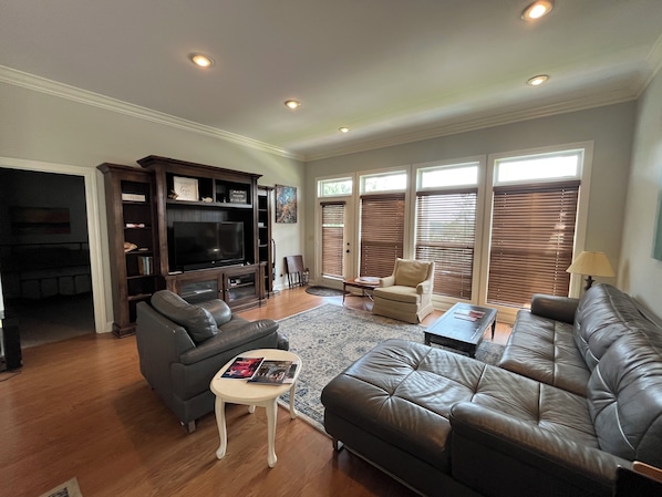 A living room with a dark leather sofa, a grey couch, a small white table, and a TV stand with shelves. - 3-Bedroom House At Safe Harbor Aqua With Lake Vew, Iuka MS (Iuka)