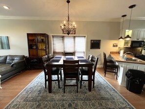 A dining area with a chandelier, a dining table with chairs, a sofa, a bookshelf, and a kitchen area with a microwave. - 3-Bedroom House At Safe Harbor Aqua With Lake Vew, Iuka MS (Iuka)