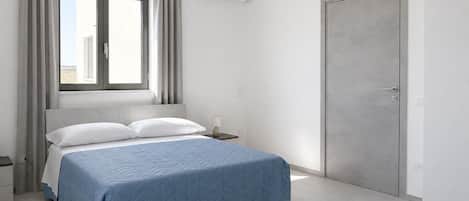 A modern bedroom with a bed, a nightstand, an air conditioning unit, and a door.