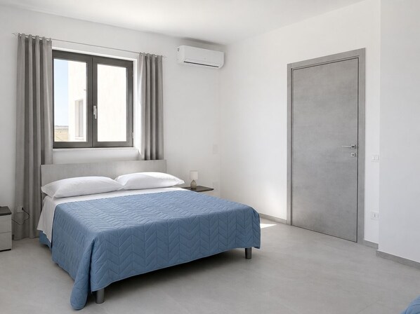 A modern bedroom with a bed, a nightstand, an air conditioning unit, and a door. - Tenuta San Tommaso Mare (Basilicata)