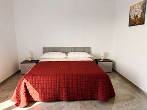 A bed with a red quilted cover, two bedside tables with lamps, and a painting on the wall. - Tenuta San Tommaso Mare (Basilicata)