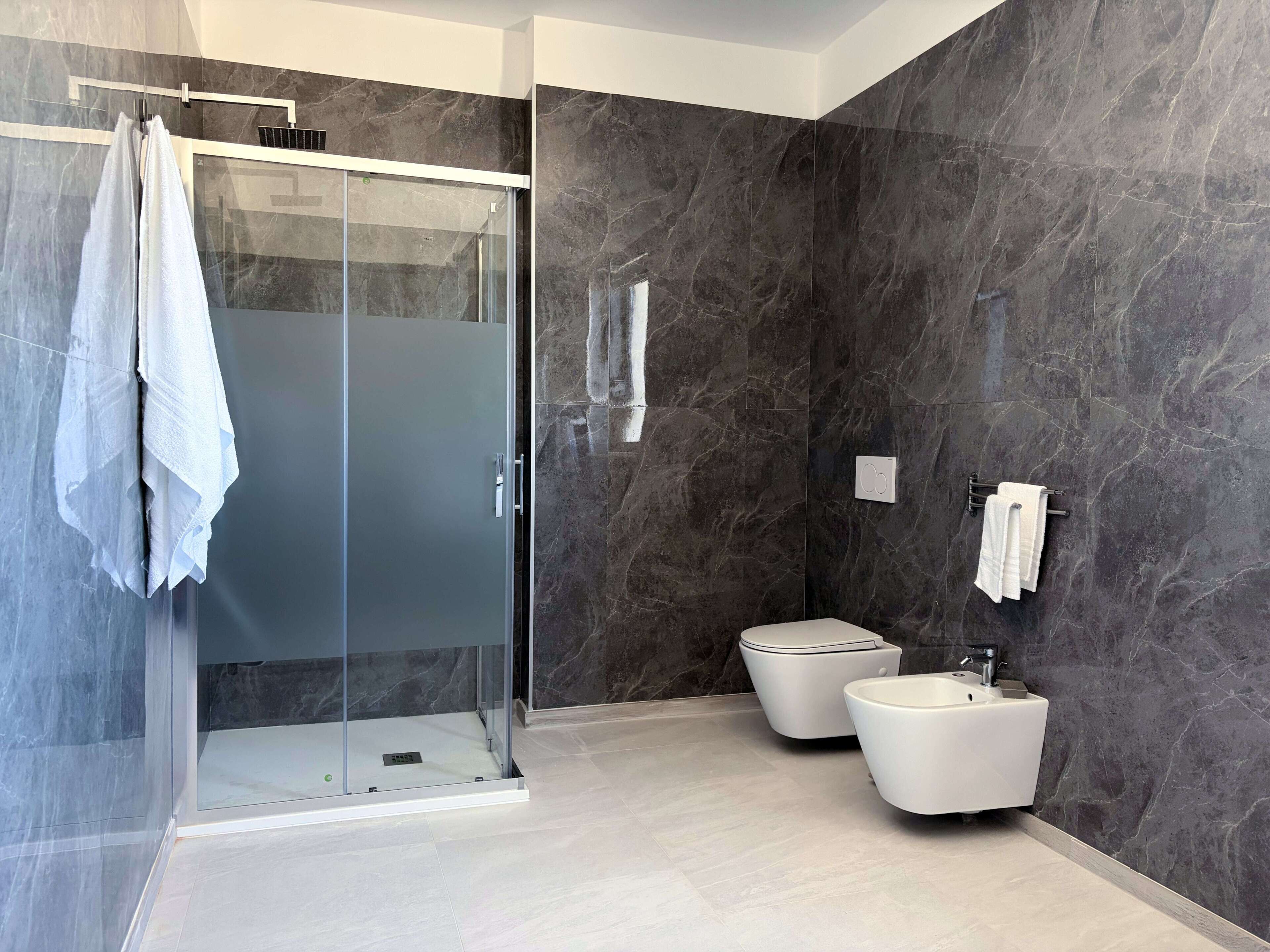 A modern bathroom with a glass shower enclosure, two toilets, and a sink.