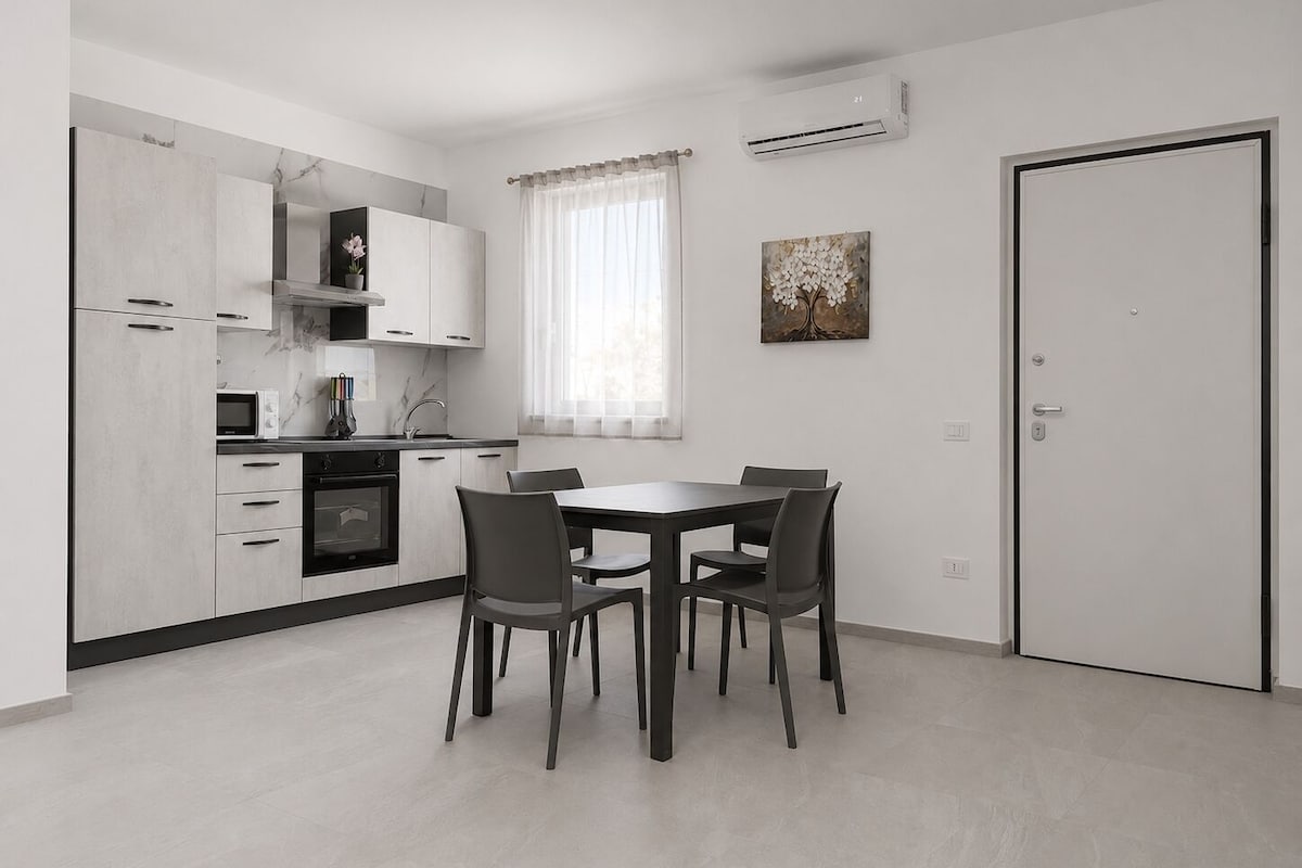 A modern kitchen with white cabinets, a dining table with four chairs, and an air conditioning unit on the wall.