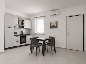 A modern kitchen with white cabinets, a dining table with four chairs, and an air conditioning unit on the wall. - Tenuta San Tommaso Mare (Basilicata)