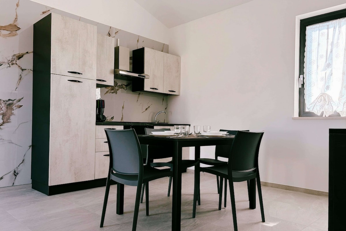 A modern kitchen with a dining table and chairs, a window with curtains, and a marble backsplash.
