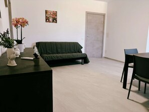 A modern living room with a dark green sofa, a dining table with chairs, a white vase with flowers, and a painting on the wall. - Tenuta San Tommaso Mare (Basilicata)