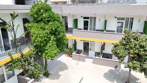 Ein mehrstöckiges Gebäude mit einem Innenhof. Mehrere Bäume und Kübelpflanzen sind vorhanden. Das Gebäude verfügt über mehrere Balkone und Fenster.