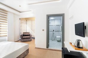 Habitació d'hotel amb llit, sofà, televisió, escriptori i paperera, i zona de banyera amb dutxa.