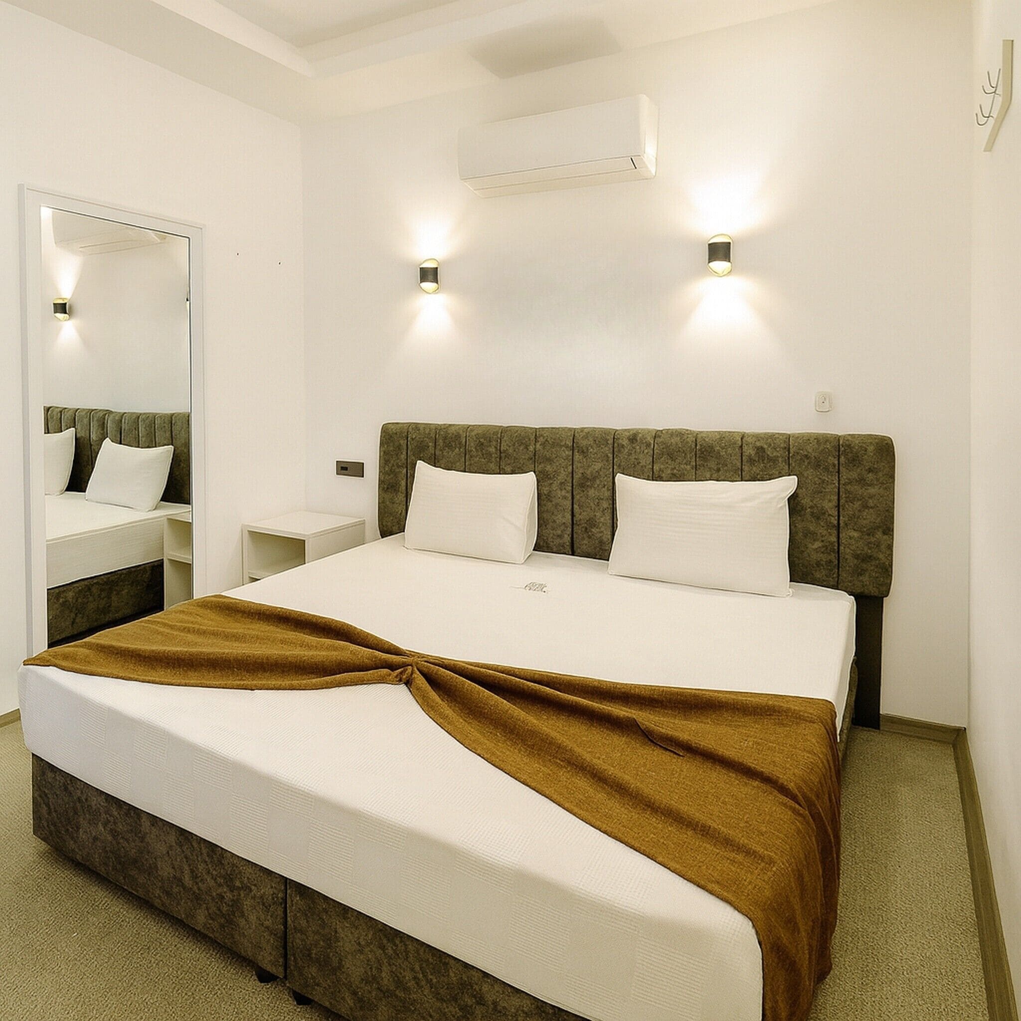 Habitación de hotel con cama, mesita de noche, espejo y dos luces fijadas a la pared.