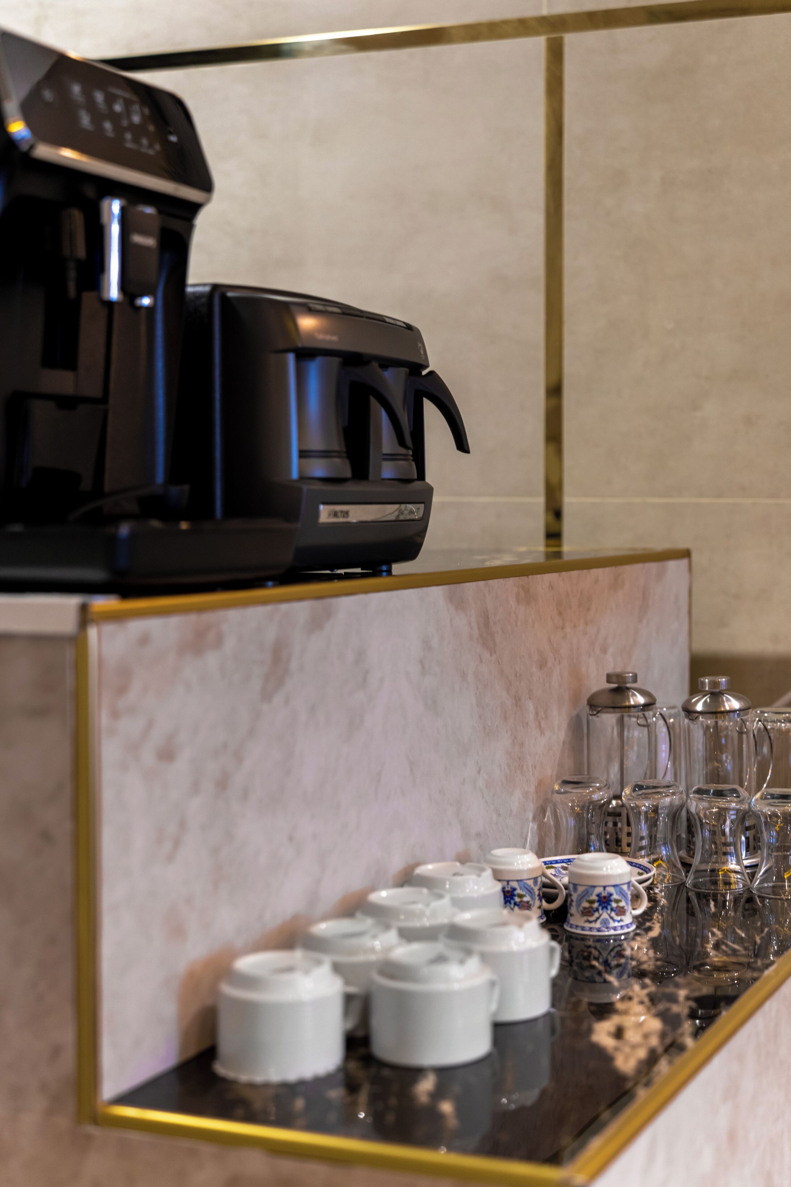 Une machine à café et un service à thé sont posés sur un comptoir en marbre, encadré d’une baguette dorée.