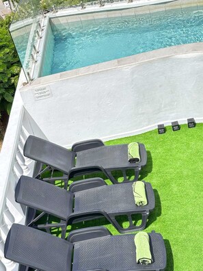 Un espace aménagé au bord de la piscine, comprenant une piscine, un ensemble de chaises et une petite portion de gazon synthétique.