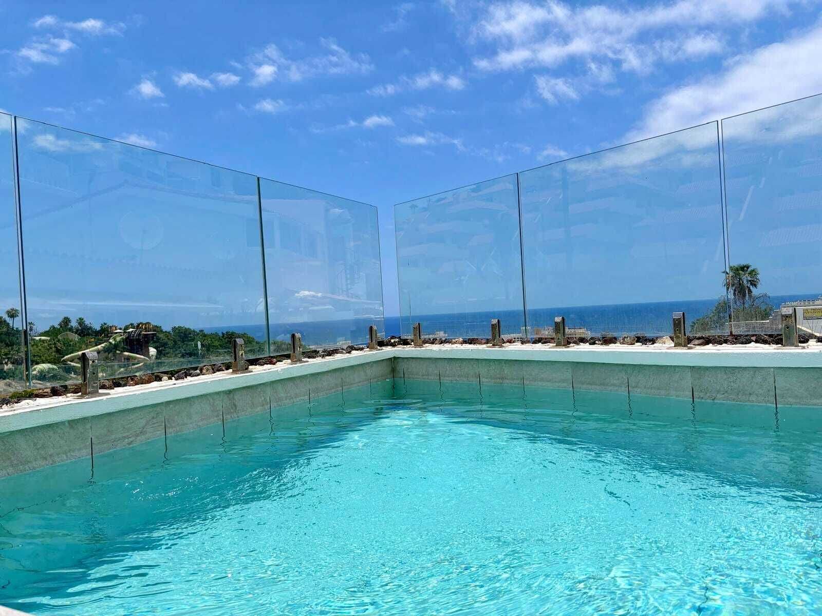 Ein klares, blaues Schwimmbecken mit Glasabgrenzung, umgeben von einer Betonplattform und Blick auf den Ozean.