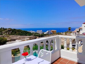 Un balcon avec une table dressée pour le dîner, offrant une vue sur un paysage urbain côtier avec ses bâtiments et la mer.