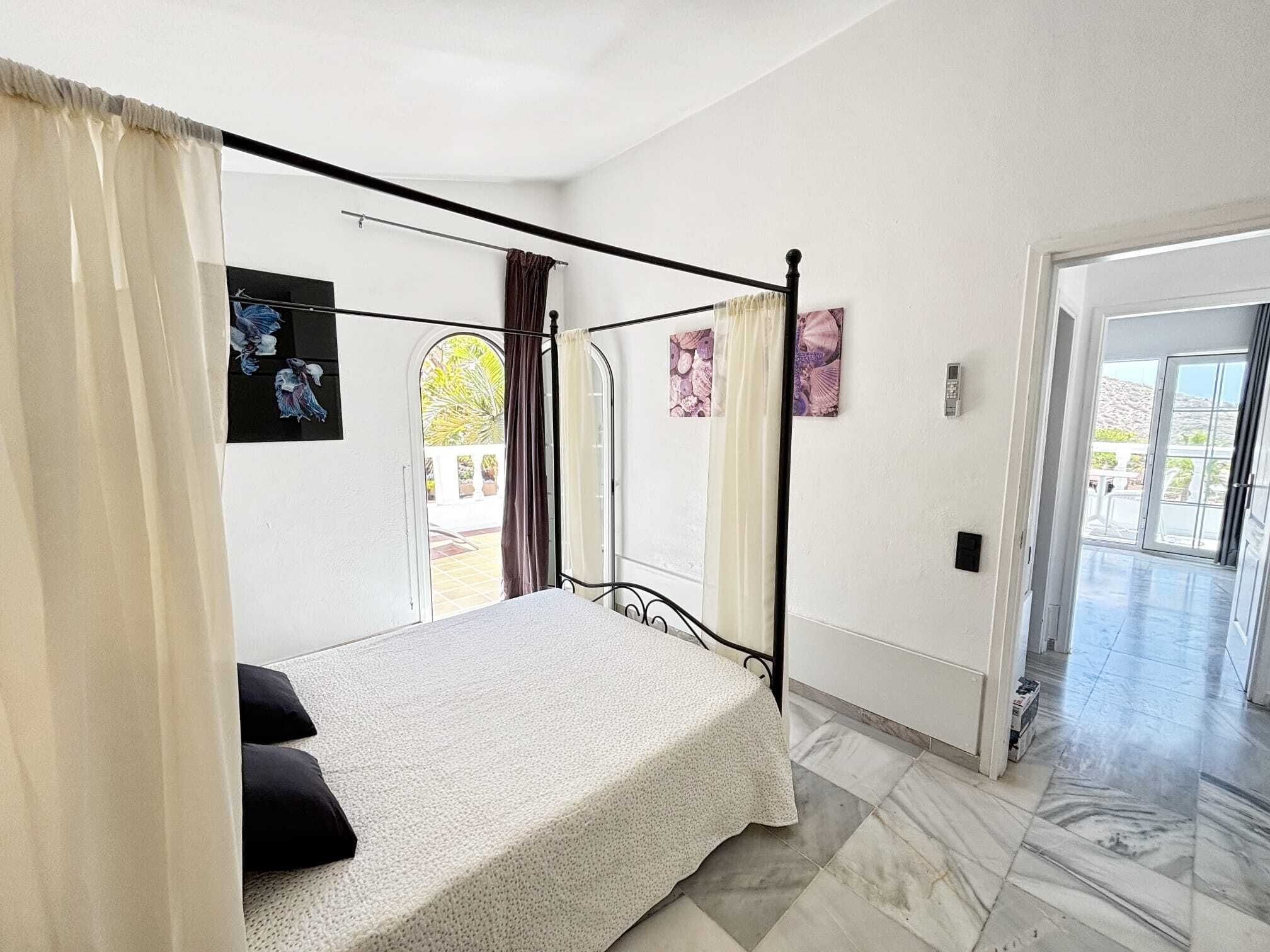 A bedroom with a four-poster bed, a door leading to a balcony, and artwork on the walls.